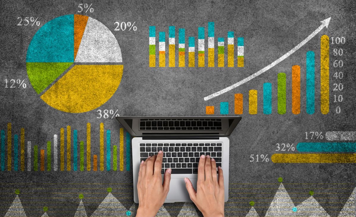 Hands typing on a computer with a background of graphs